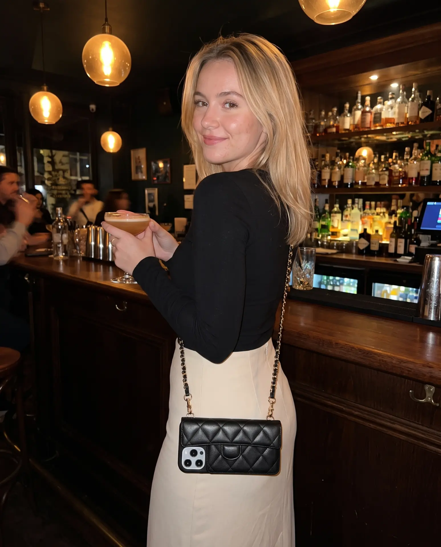Midnight Black phone purse with a short pocket resting on a dark wooden bar counter under warm globe lights