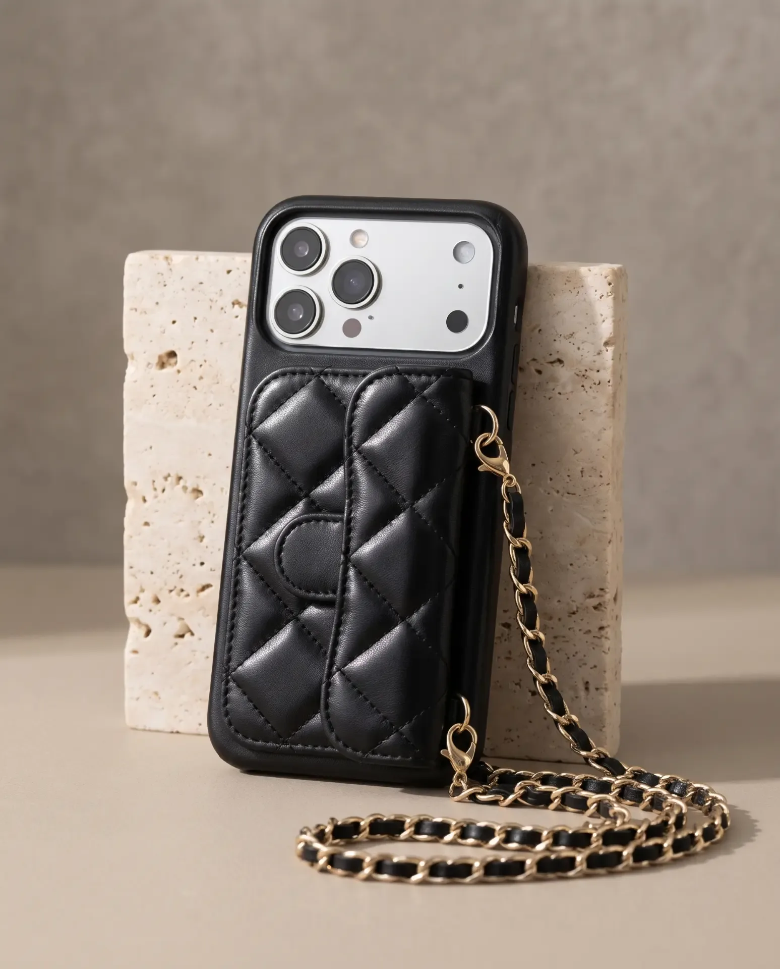 Midnight Black phone purse with a short pocket, standing against a travertine block with its gold chain in front