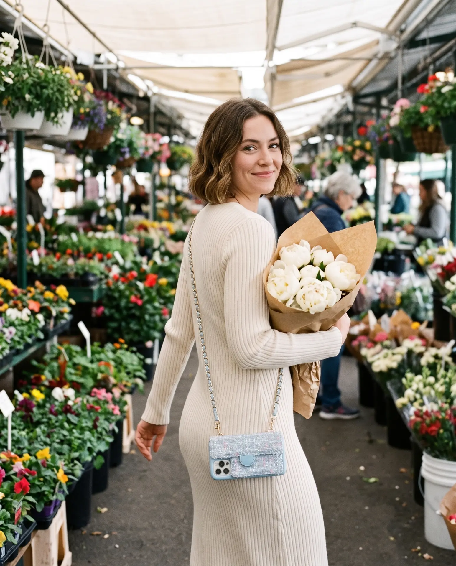 Sky Blue Tweed phone purse with a full-length pocket worn crossbody at a flower market, holding a bouquet of white peonies