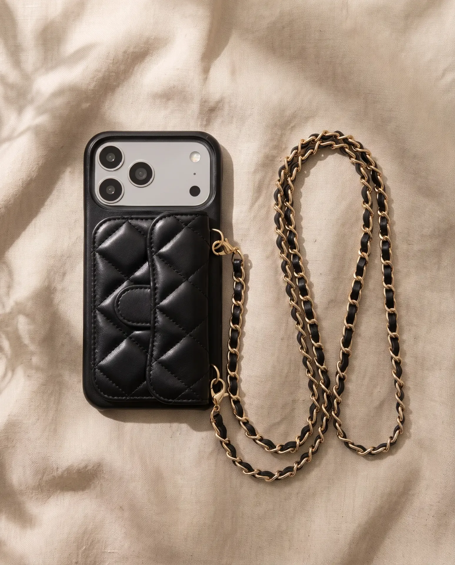 Midnight Black phone purse with a short pocket, laid flat on wrinkled beige linen with its gold chain curving beside it