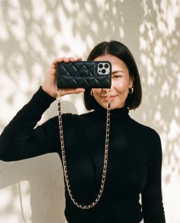 A black phone purse held up against a sunlit wall