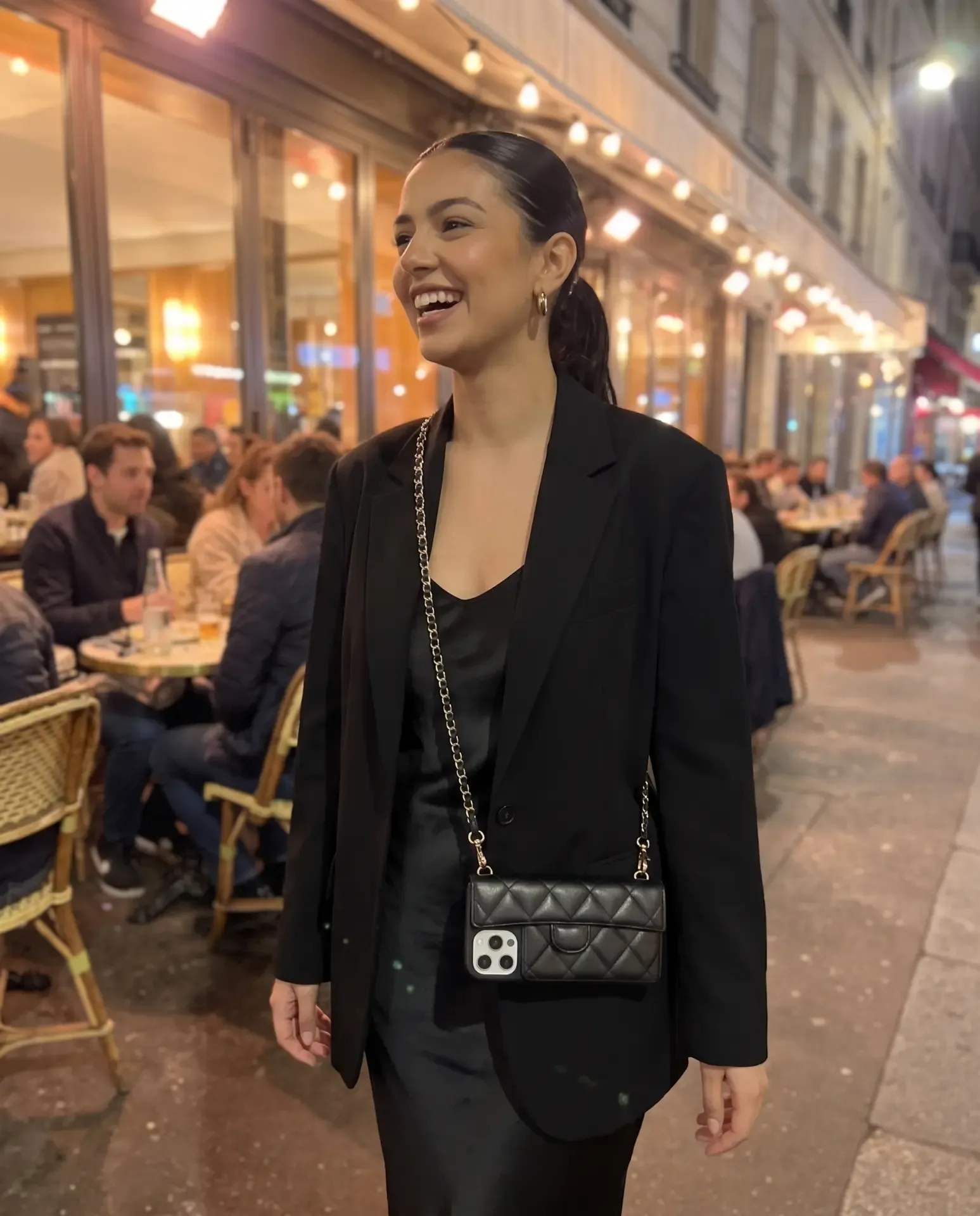 Midnight Black phone purse with a short pocket held on an outdoor café terrace at night, warm lights and diners behind