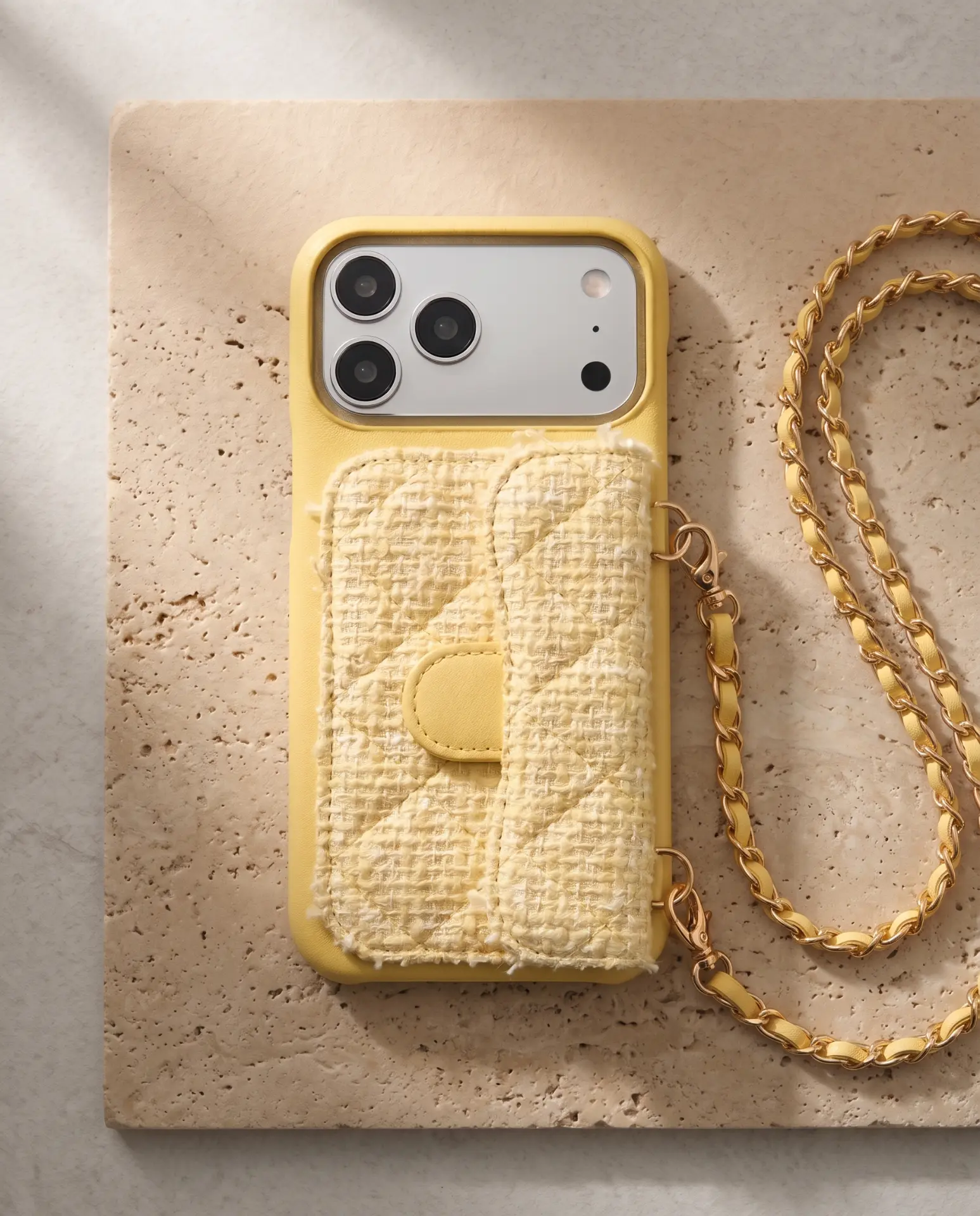 Lemon Tweed phone purse with a short pocket, laid flat on a limestone slab with its gold chain beside it