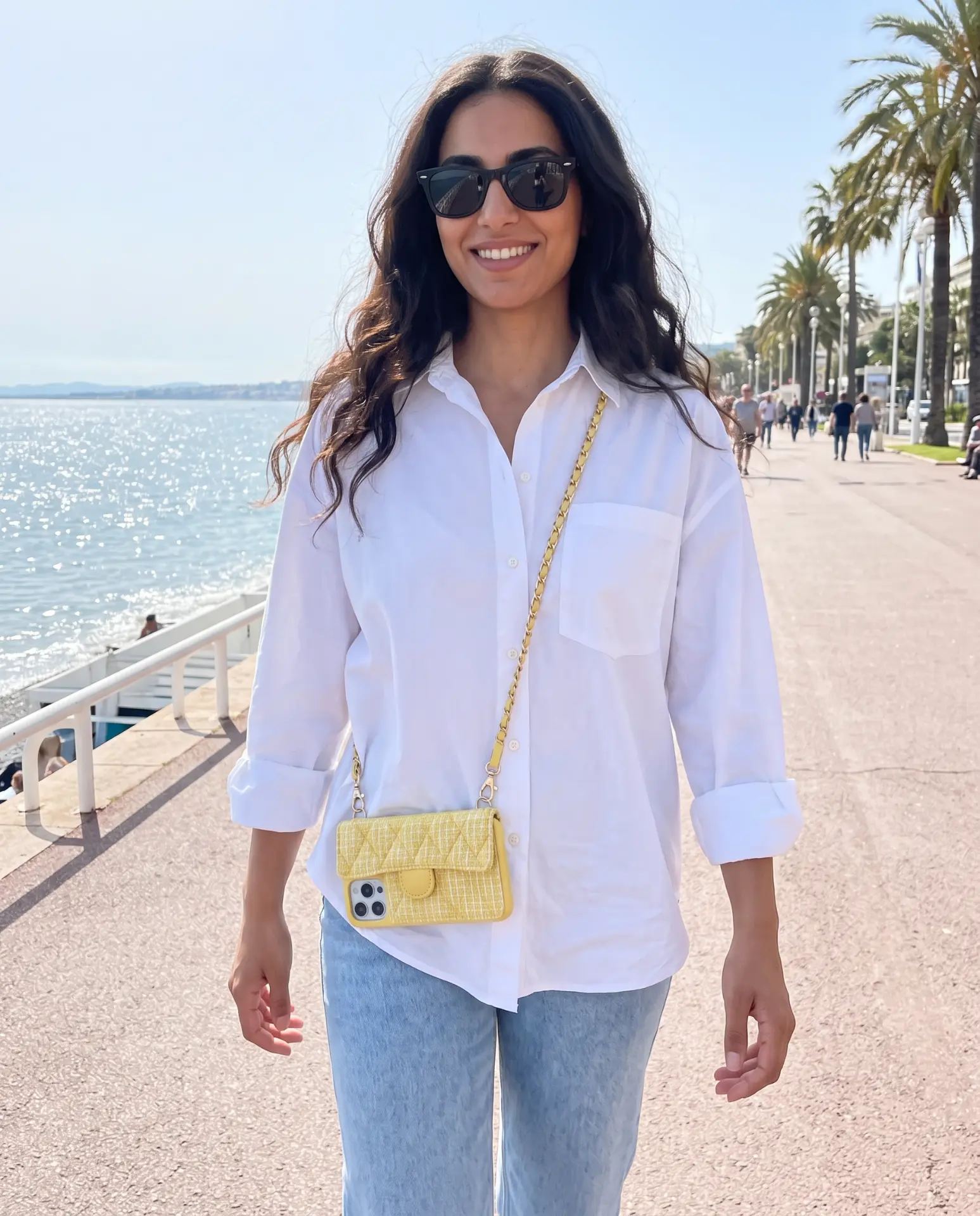 Lemon Tweed phone purse with a full-length pocket held on a sunny seaside promenade lined with palm trees
