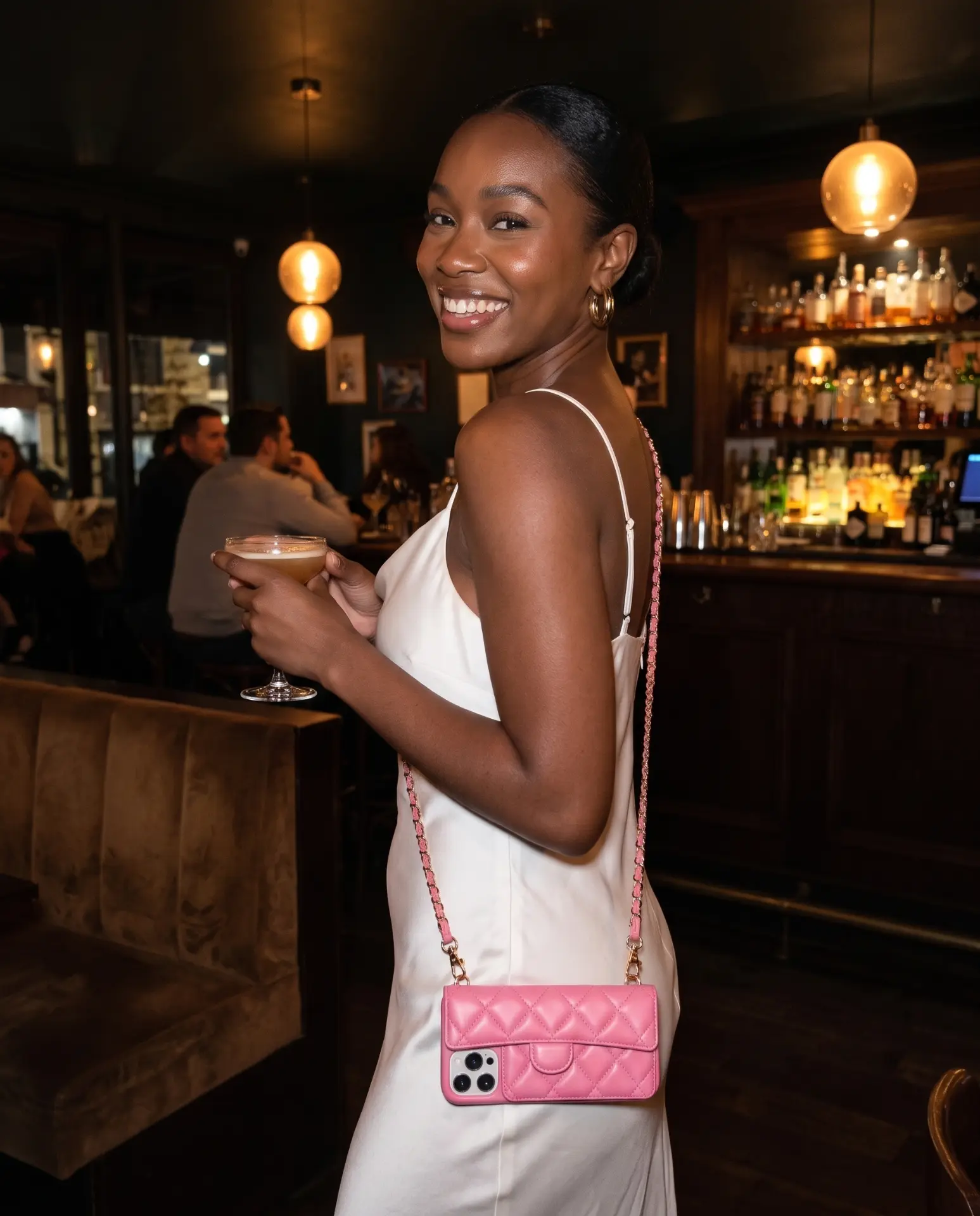Powder Pink phone purse with a full-length pocket on a dark wooden bar counter under warm pendant lights