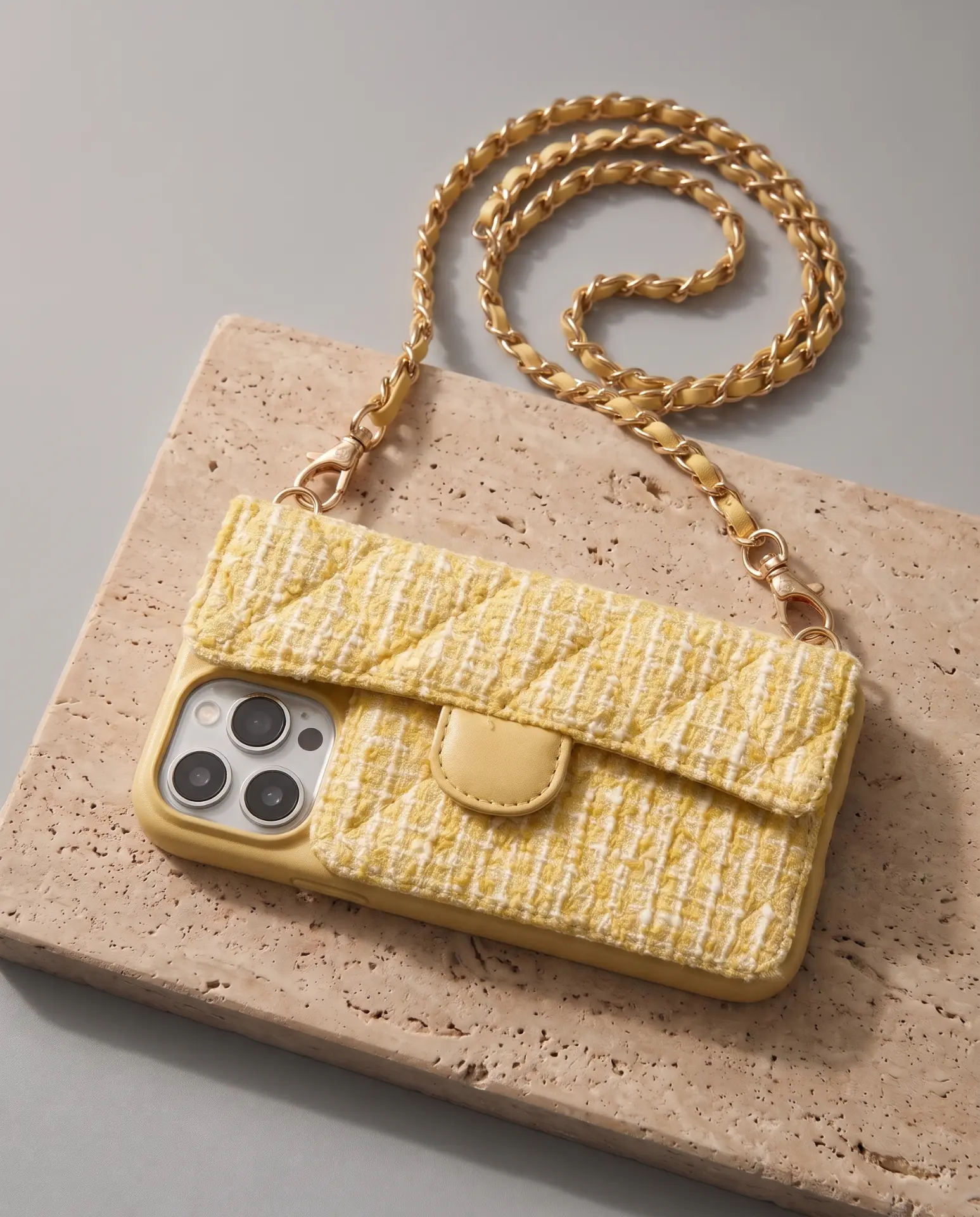 Lemon Tweed phone purse with a full-length pocket, laid flat on a travertine slab with its gold chain looping above it