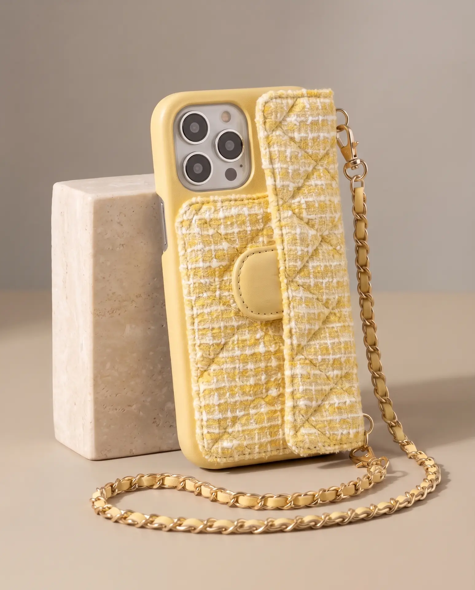 Lemon Tweed phone purse with a full-length pocket, propped upright against a travertine block with its gold chain pooling in front