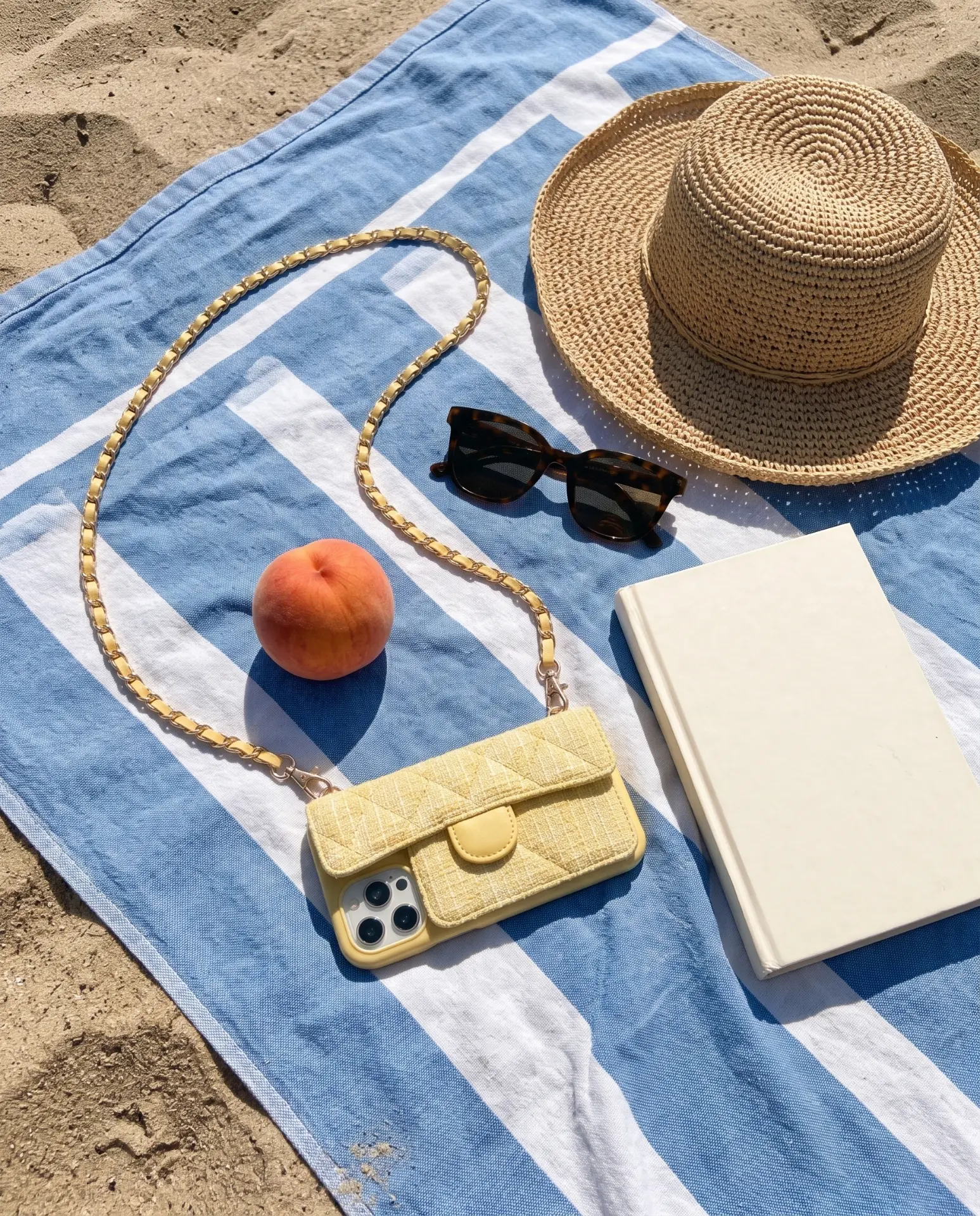 Lemon Tweed phone purse with a full-length pocket on a striped beach towel with a straw hat, sunglasses, a peach and a book