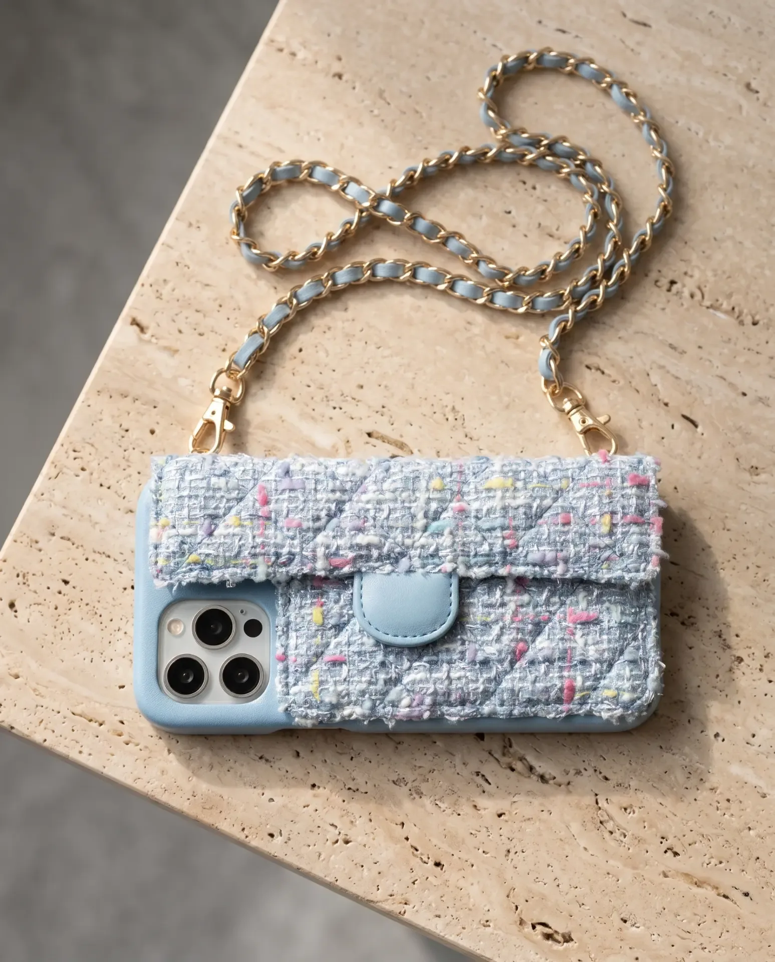 Sky Blue Tweed phone purse with a full-length pocket, laid flat on a travertine slab with its gold chain curved above it