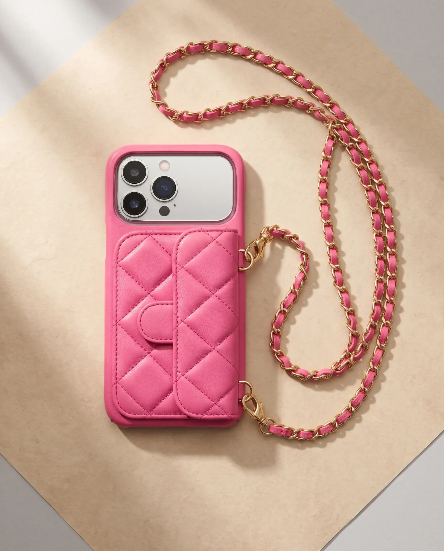 Powder Pink phone purse with a short pocket, seen from above with its gold chain on a sandy surface
