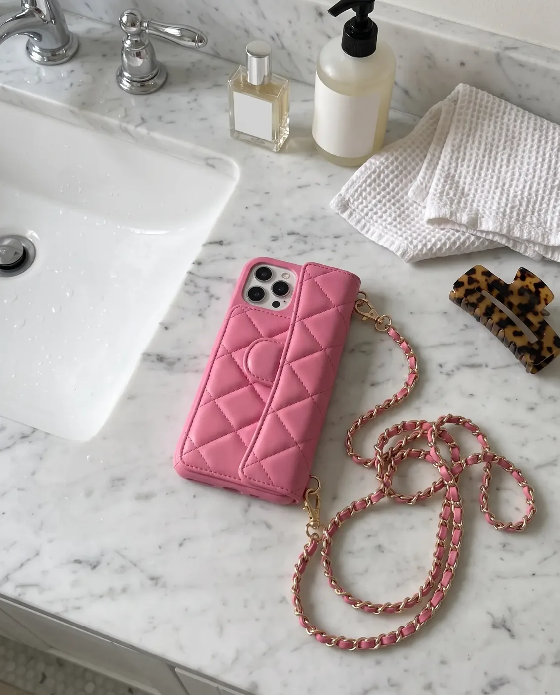 Powder Pink phone purse with a full-length pocket, on a marble bathroom vanity beside a sink with folded white towels and a perfume bottle