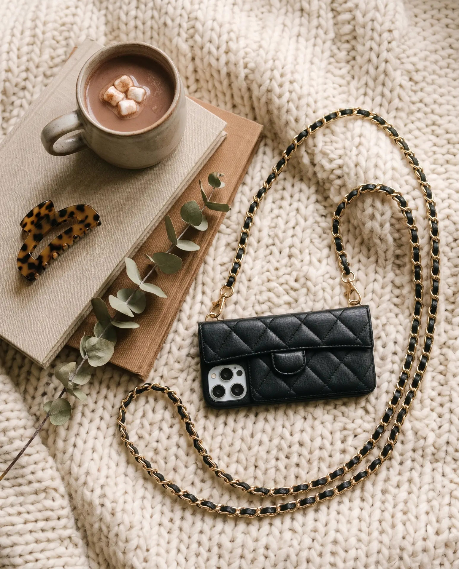 Midnight Black phone purse with a full-length pocket on a chunky knit blanket beside a hot chocolate, books and a tortoiseshell clip