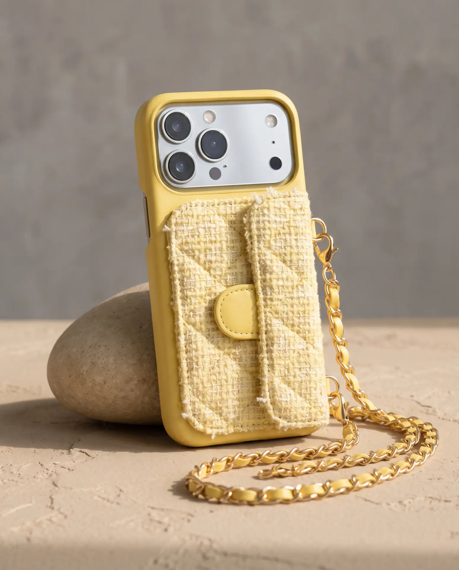 Lemon Tweed phone purse with a short pocket, propped against a river stone with its gold chain